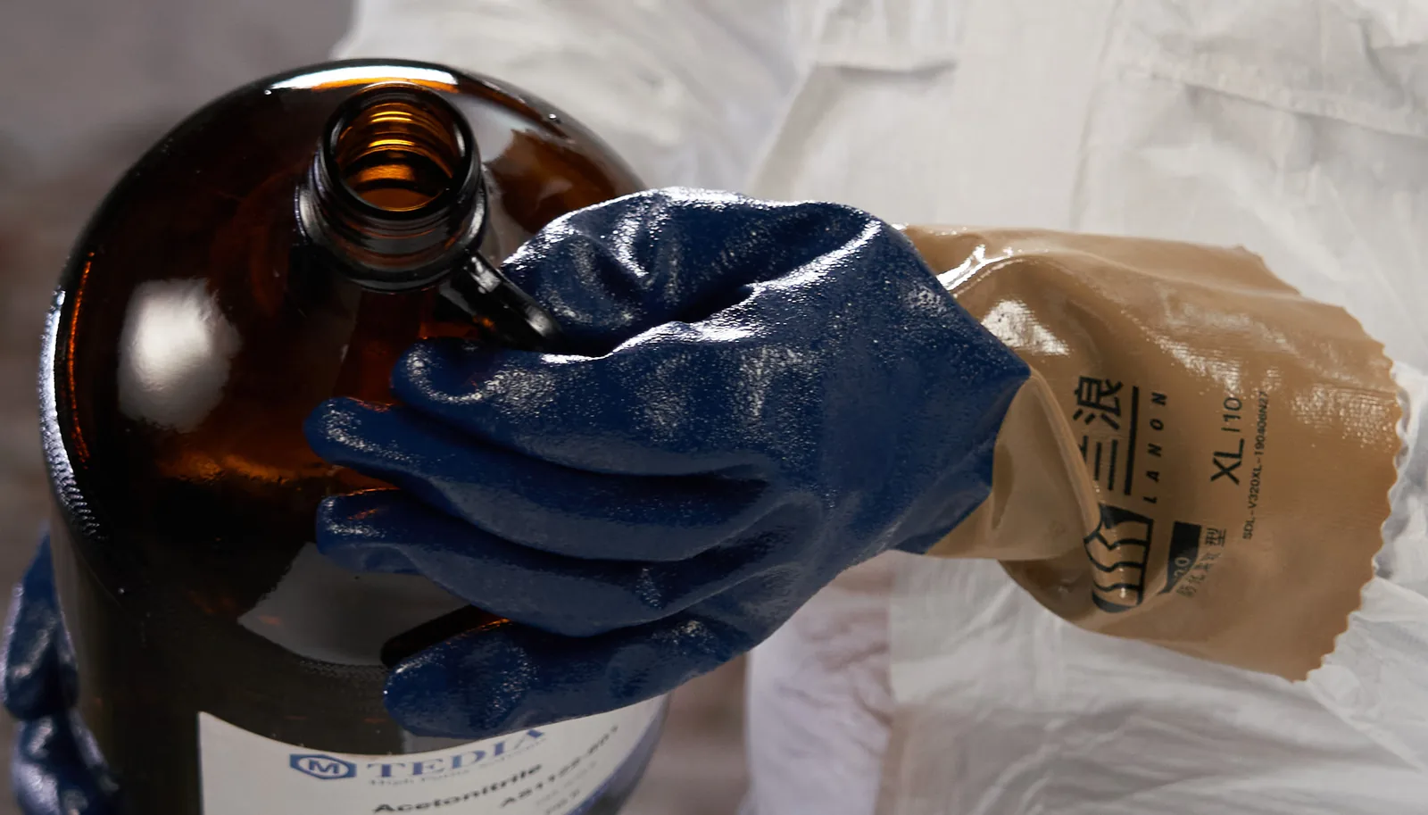 Blue 338-series nitrile gloves handling an industrial liquid container